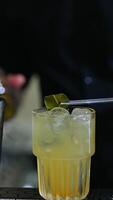 Making cocktails on the bar stand. Male bartender putting a green leaf into a glass filled with ice and beverage. Close up. Blurred backdrop. Vertical video