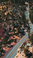 Mountainous wooded territory with road going along it. Pine tree forest growing on rocks. Top view. Vertical video