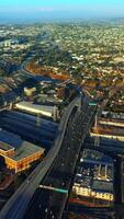 Lively traffic on the highways of Los Angeles at daytime. Sunny panorama of the city at backdrop of mountains. Top view. Vertical video