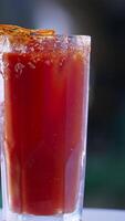 Red cocktails in a high glass with salt crystals on top. Rotating beverage with a slice of dried orange on top. Close up. Blurred backdrop. Vertical video