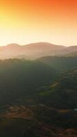 Bright sun lighting the mountainous landscape covered with greenery. Hazy rocky silhouettes at backdrop of pink and orange sky. Vertical video