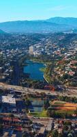 Approaching the beautiful little lake in the residential area of Los Angeles. Busy traffic in the green part of the city at backdrop of mountains. Vertical video