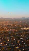 Hot air balloons flying over the beautiful city. Sunlit scenery of Napa, California, USA at the backdrop of hazy mountains. Top view. Vertical video
