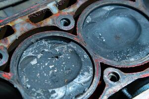An exposed disassembled internal combustion engine. The engine block contains dirty pistons with carbon deposits and broken pieces of metal. The concept of lack of car care and untimely engine service photo