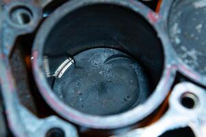 An exposed disassembled internal combustion engine. The engine block contains dirty pistons with carbon deposits and broken pieces of metal. The concept of lack of car care and untimely engine service photo