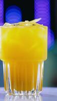 A glass filled to the top with beverage of yellow color. Savory cocktail on the rotating table close up. Blurred backdrop. Vertical video