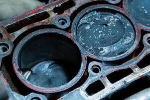 An exposed disassembled internal combustion engine. The engine block contains dirty pistons with carbon deposits and broken pieces of metal. The concept of lack of car care and untimely engine service photo