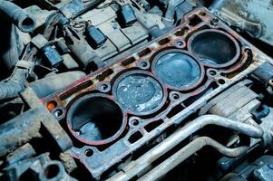 An exposed disassembled internal combustion engine. The engine block contains dirty pistons with carbon deposits and broken pieces of metal. The concept of lack of car care and untimely engine service photo