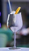 Misted metal wineglass with metal straw inside on the rotating table. Cocktail with ice cubes and orange slice on top. Close up. Blurred backdrop. Vertical video