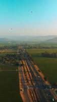 Stunning beautiful green valley with some vineyards. Hot air balloons in blue sky over the land. Hazy mountains at backdrop. Vertical video