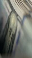 A number of hundred dollar bills with Benjamin Franklin portrait moving into money counting machine. Equipment for cash operations. Close up. Vertical video