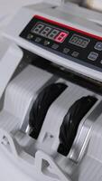 Hand puts a pack of fifty euro bills into money counting equipment. Machine for calculating currency at work close up. Blurred backdrop. Vertical video