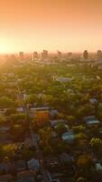 Last rays of setting sun over the beautiful green city. Few multi-storied buildings standing out at the backdrop of orange sky. Vertical video