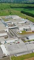 Exterior of modern manufacturing in nature. Large industrial complex with car parking among the environment in summer. Motion top down. Vertical video
