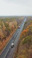 Road works on one side of highway in autumn. Aerial view of asphalt road with cars with colorful trees from both sides of a road. Vertical video
