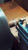A detail is cutting with using a rotating lathe producing remnants of metal shavings in the plant. Close-up. Vertical video