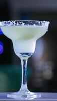 Glass goblet on the little rotating table. Light beverage with a piece of lime inside. Close up. Blurred backdrop. Vertical video
