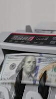 Man puts a wad of USD dollars into cash counting equipment. Banknotes with Benjamin Franklin portrait turning in the machine. Close up. Vertical video