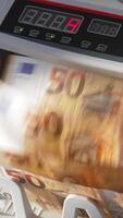 Electronic cash counting machine counts fifty euro banknotes. Figures changing quickly on the counter display at backdrop in blur. Close up. Vertical video