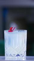 Old-fashioned glass with drink on the rotating table. Cocktail decorated with red flower in the bar. Close up. Blurred backdrop. Vertical video