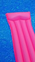Long pink inflatable mattress in the blue water. Mattress drifting by the water in the swimming pool. View from top. Vertical video