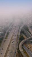 Wavy complicated roads going to the thick fog. Numerous cars riding by the highways on foggy daytime. Top view. Vertical video