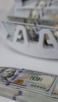 A wad of one hundred dollar bills lies on the table. Cash counting machine counts one hundred dollar bills at backdrop. Close up. Vertical video