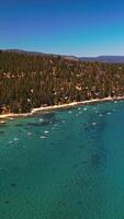 Beautiful azure water of Lake Tahoe with many boats on. Green pine trees overgrowing the rocky shore. View from top. Vertical video