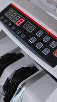 Male hand inserts a wad of hundred dollar bills into a slot of cash counting machine. Equipment for financial operations close up. Blurred backdrop. Vertical video