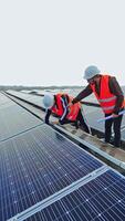Solar panels installation. Two workers in a uniform and hard hat install photovoltaic panels on a solar farm. Innovative electricity system. Vertical video