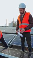 Workers installing solar panels. Sustainable green energy. Men technicians in protective uniform working with solar panels outdoors. Vertical video