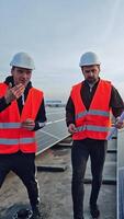 Solar panels for a renewable energy. Workers in protective orange uniform talking on the big power station with solar panels. Vertical video