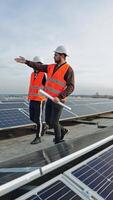 Solar energy farm under the sky. Technicians in protective uniform coming among sunny batteries and talking about alternative source of energy. Vertical video