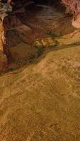 Sandy ground with scarce greenery among the huge canyons. Rocky lifeless scenery at the backdrop of blue cloudy skies. Aerial view. Vertical video