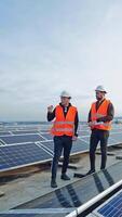 Blue solar panels on the field. Workers in the protective uniform on the modern photovoltaic farm. Alternative energy. Vertical video
