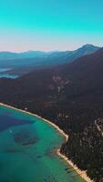Terrific high mountains with beautiful lake at its foot. Huge rocks overgrown with pine trees. Lake Tahoe at the backdrop of azure sky. Vertical video