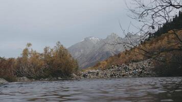 A quick shot of the river in the wind. Creative. Yellow trees with foliage and high mountain hills with walking tourists. video