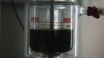 Rotating dark liquid in laboratory flask. Stock footage. Bubbling liquid in flask with installation for chemical experiment. Chemical experiment with liquid in flask and rotation or heating video