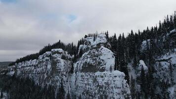 Aerial winter snow scene with ice covered cliff. Clip. White cliff edge with forested top. video