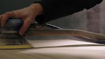 Close-up of master polishing wooden board. Creative. Polishing machine in hands of woodworking master. Man polishes wooden table with machine in workshop video