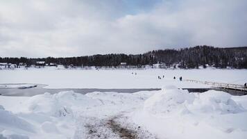 View of clearing with lake and vacationing people in winter. Clip. Road to winter glade with river and people walking in winter. Snow field with river and clearing for vacationers in winter video