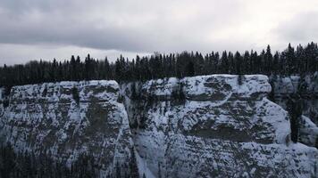 Aerial winter snow scene with ice covered cliff. Clip. White cliff edge with forested top. video