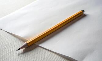 A simple yellow pencil is lying on an empty piece of paper photo