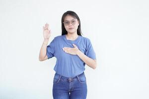 Beautiful Asian woman places her hand on her chest, making a sincere gesture of an oath or promise against a white background photo