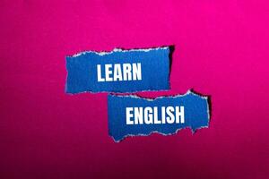 Learn english message written on ripped torn blue paper pieces with pink background. Conceptual learn english symbol. Copy space. photo