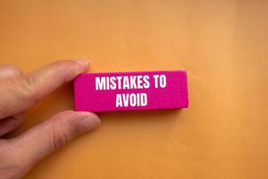 Mistakes to avoid message written on pink wooden block with orange background. Conceptual mistakes to avoid symbol. Copy space. photo