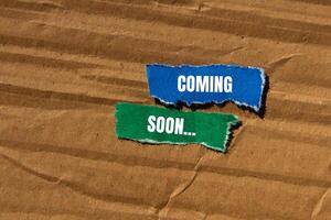 Coming soon message written on ripped torn paper pieces with cardboard background. Conceptual coming soon symbol. Copy space. photo