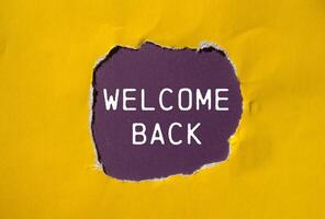 Welcome back message written on ripped torn yellow paper with purple background. Conceptual welcome back symbol. Copy space. photo