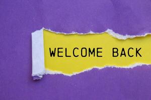 Welcome back message written on ripped torn purple paper with yellow background. Conceptual welcome back symbol. Copy space. photo