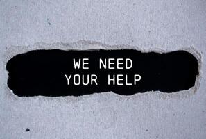 We need your help message written on ripped torn gray paper with black background. Conceptual We need your help symbol. Copy space. photo